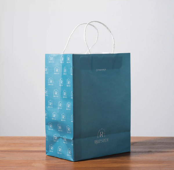 A mockup of a full color white kraft paper bag is displayed on a gray background and wood grain tabletop